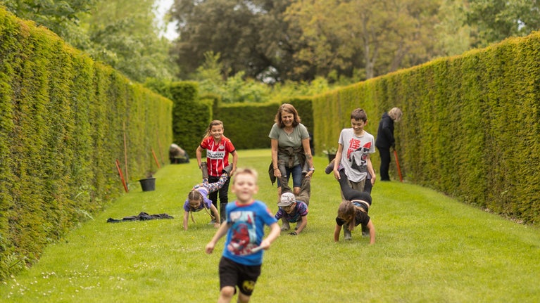 Family running and playing wheelbarrows in the garden, Lytes Cary Manor, Somerset